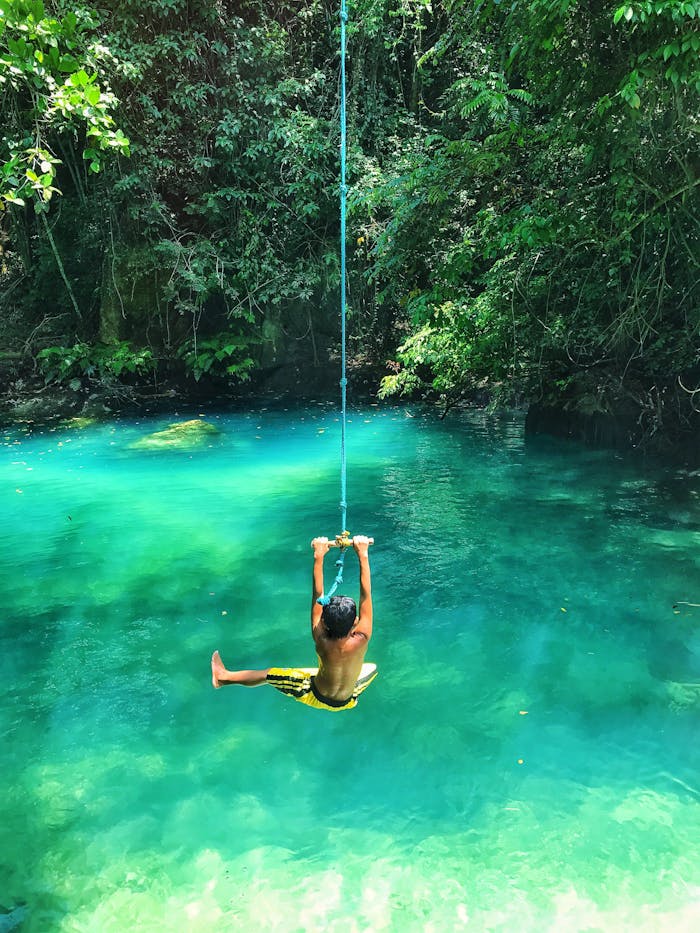 A child swinging joyfully on a rope over a stunning turquoise tropical lagoon.