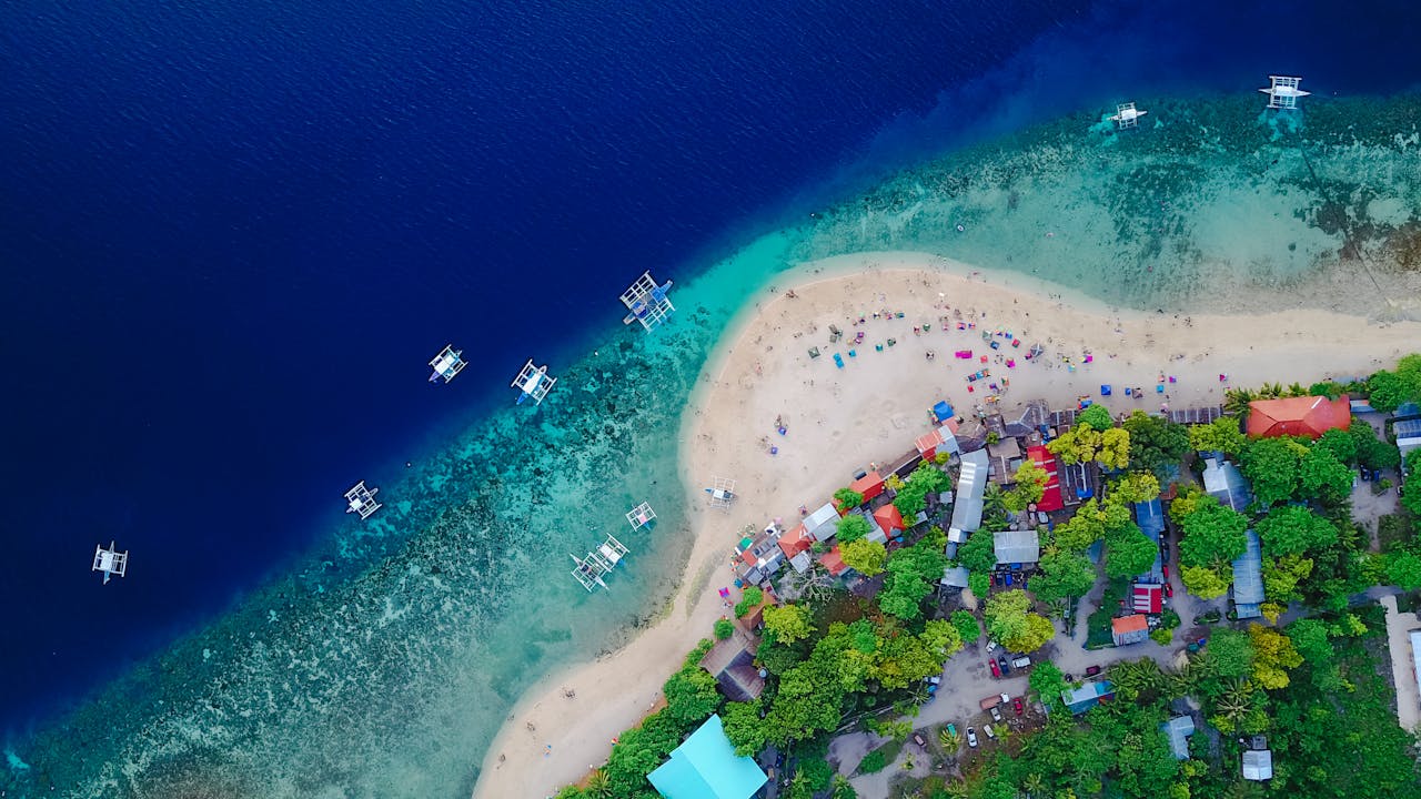 A stunning aerial view of Oslob Beach, Cebu, with vibrant blue waters and lush greenery.