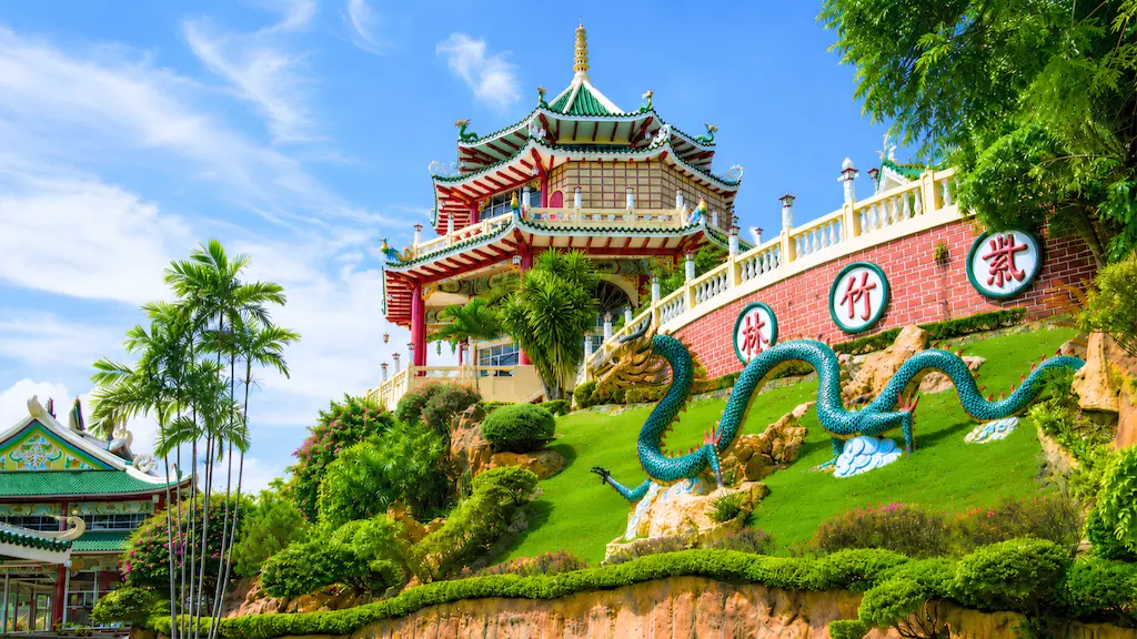 A multi tiered Chinese pagoda temple and a large green dragon statue on a grassy hill at the Cebu Taoist Temple along the scenic Cebu highlands route