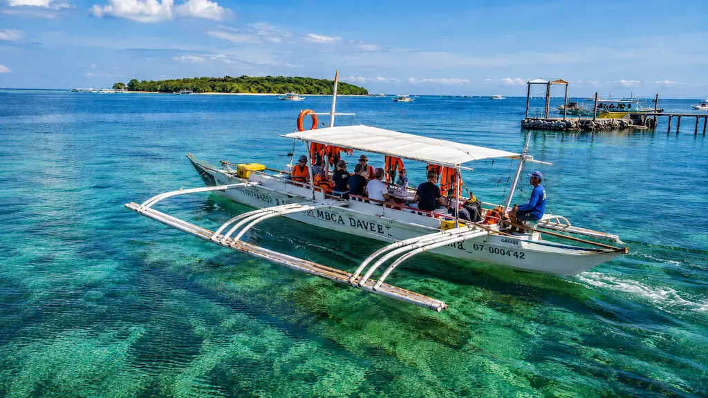 A traditional motorized outrigger boat carrying tourists over clear turquoise ocean water during a Mactan island hopping tour in Cebu