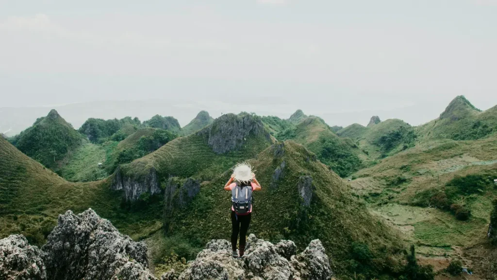 A hiker with a backpack looking out at the unique jagged green hills from the rocky summit of Osmeña Peak Dalaguete Cebu