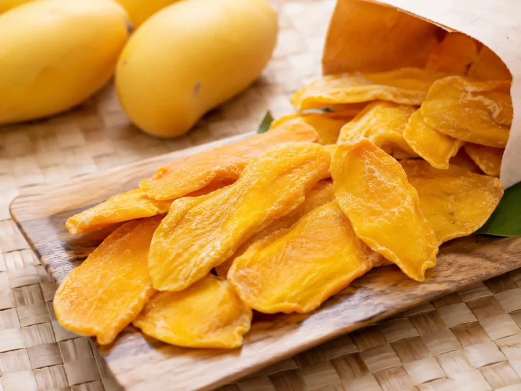 Cebu dried mango slices arranged on a wooden tray with fresh mangoes in the background.
