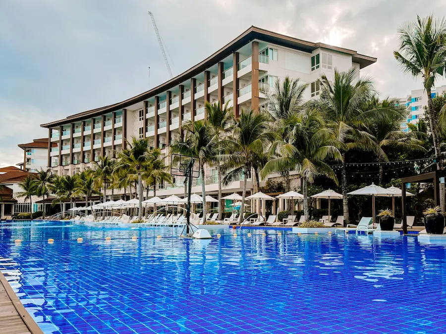 Dusit Thani Mactan Cebu Resort with a large swimming pool, palm trees, lounge chairs, and the resort building in the background.